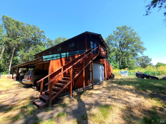 rear view of property featuring a garage, stairs, driveway, a wooden deck, and a carport