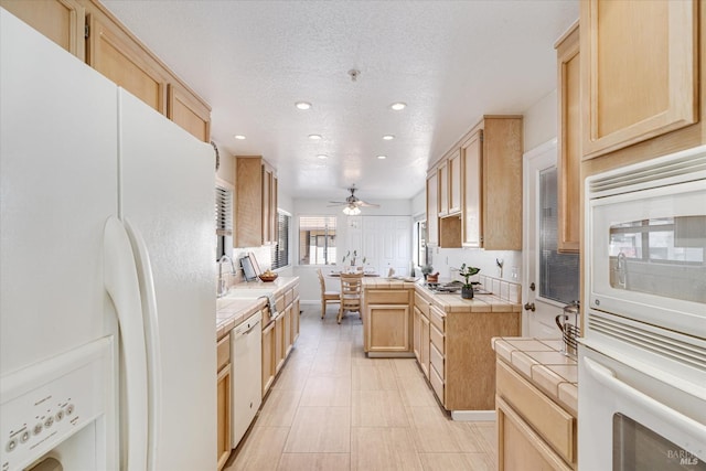 kitchen featuring a textured ceiling, white appliances, a ceiling fan, tile counters, and light brown cabinetry