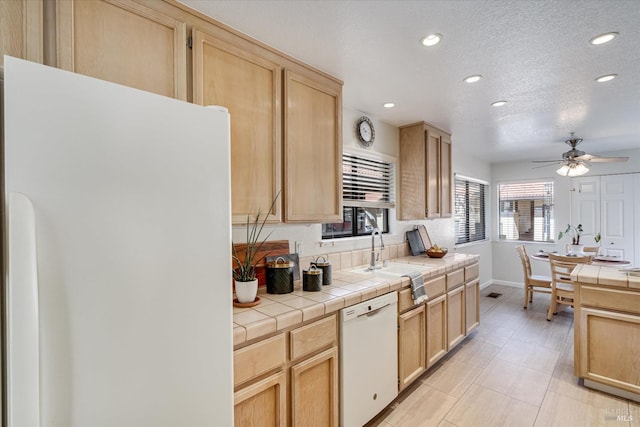 kitchen with tile countertops, light brown cabinetry, and white appliances