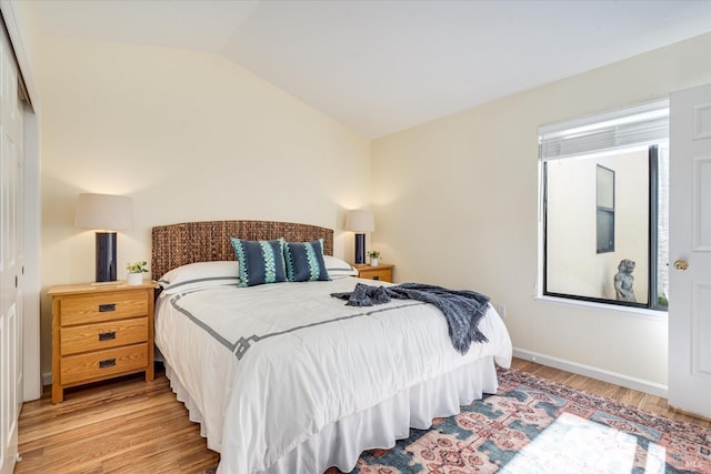 bedroom featuring lofted ceiling, baseboards, and light wood-style floors