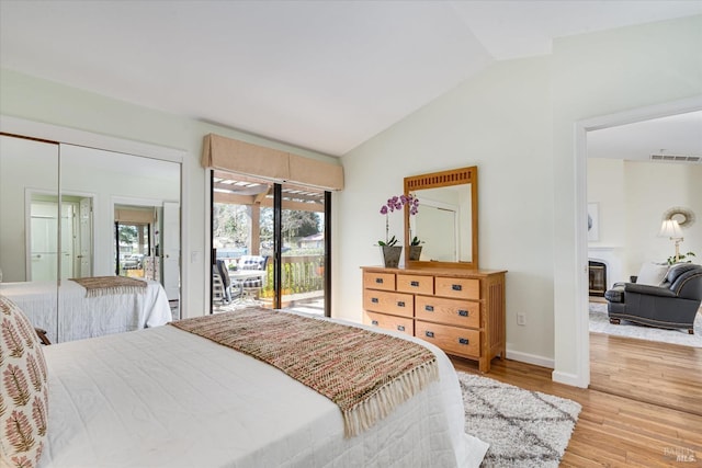 bedroom with visible vents, a glass covered fireplace, lofted ceiling, light wood-style flooring, and access to exterior