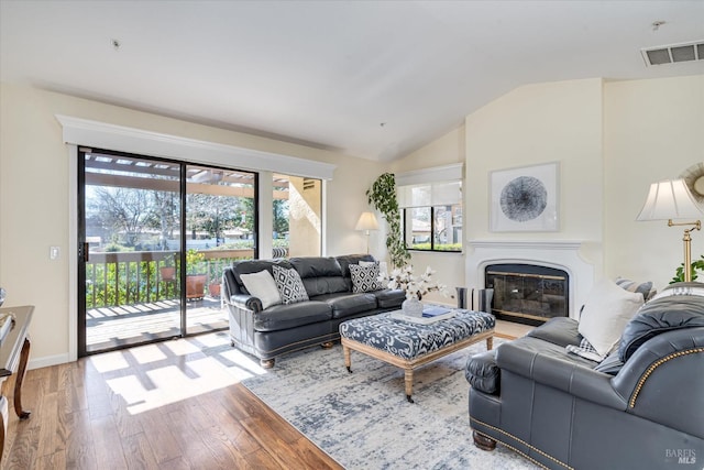 living area featuring lofted ceiling, visible vents, wood finished floors, and a glass covered fireplace