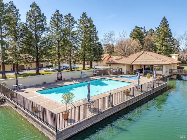 pool featuring a water view, a patio area, and fence