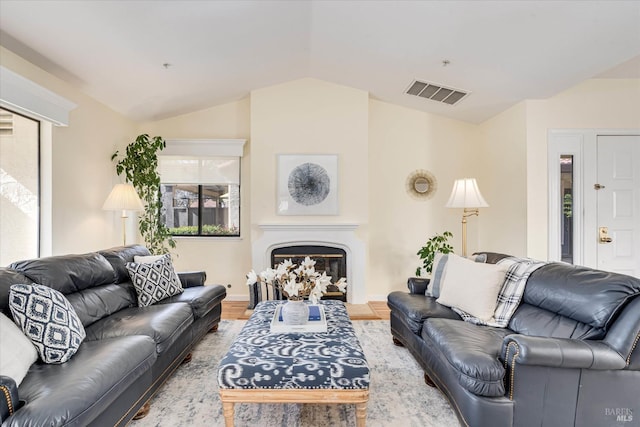 living room featuring lofted ceiling, visible vents, a glass covered fireplace, and wood finished floors