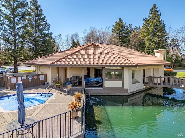 back of house with a tiled roof, a community pool, a patio, and stucco siding