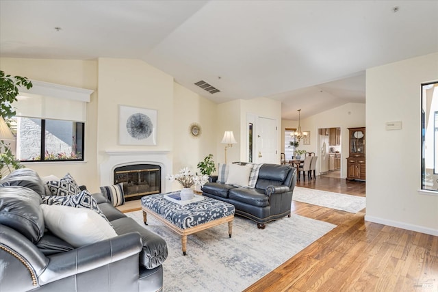 living area featuring lofted ceiling, a glass covered fireplace, visible vents, and light wood finished floors