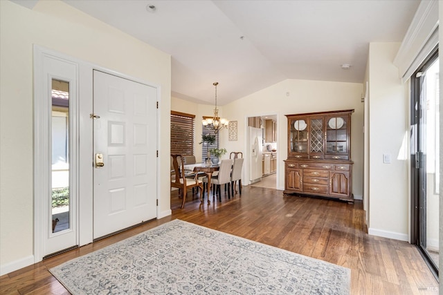 foyer entrance with an inviting chandelier, a wealth of natural light, vaulted ceiling, and dark wood-type flooring