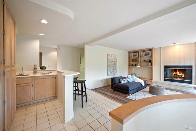 interior space featuring open floor plan, a large fireplace, a sink, light tile patterned flooring, and a peninsula