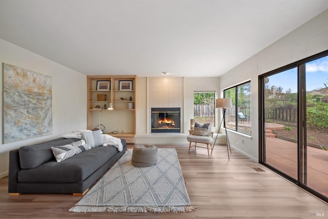 living area with baseboards, a glass covered fireplace, and light wood-style floors