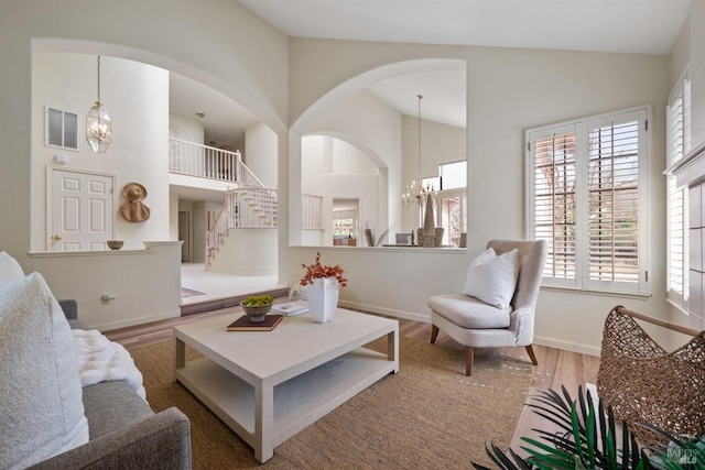 living room featuring a notable chandelier, visible vents, wood finished floors, high vaulted ceiling, and stairs