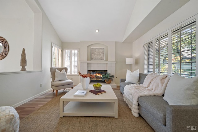 living area with vaulted ceiling, a fireplace, wood finished floors, and baseboards