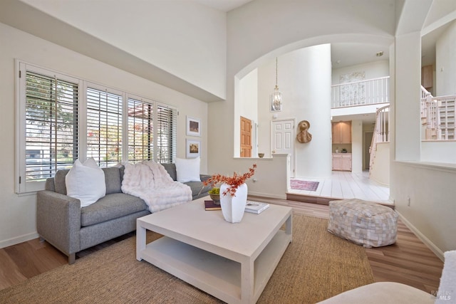 living area with arched walkways, a towering ceiling, baseboards, and wood finished floors