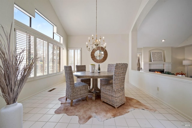 tiled dining space featuring baseboards, visible vents, a chandelier, a tiled fireplace, and high vaulted ceiling