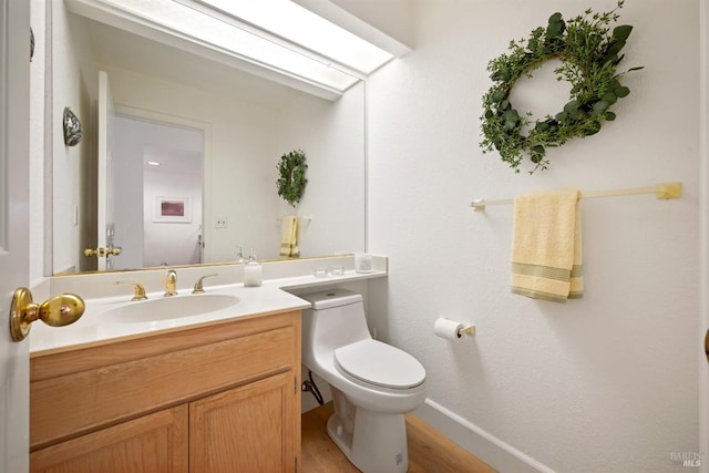 half bathroom with a skylight, toilet, vanity, wood finished floors, and baseboards