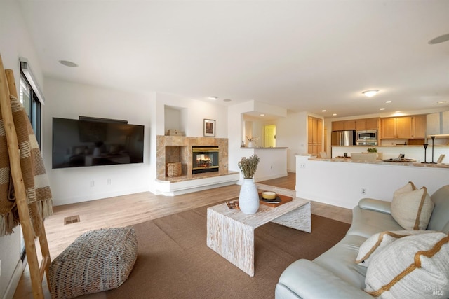 living room with a tile fireplace, recessed lighting, visible vents, baseboards, and light wood finished floors