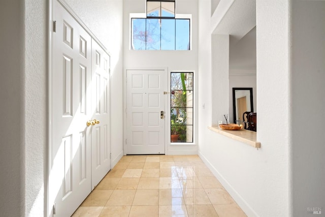 foyer with light tile patterned floors, a high ceiling, and baseboards