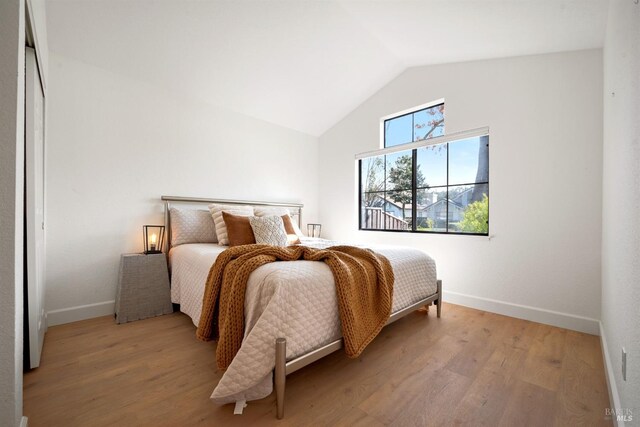 bedroom with vaulted ceiling, light wood-style flooring, and baseboards