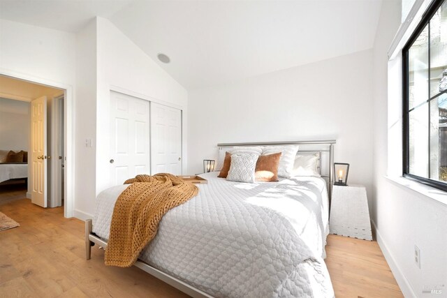 bedroom featuring light wood-type flooring, a closet, vaulted ceiling, and baseboards