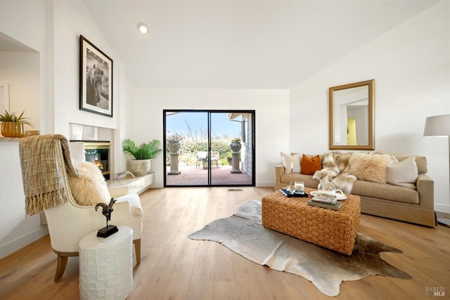 living area featuring lofted ceiling, baseboards, a glass covered fireplace, and light wood finished floors