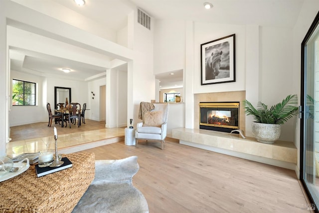 sitting room with wood finished floors, a towering ceiling, visible vents, baseboards, and a tiled fireplace