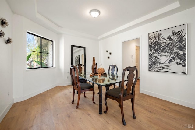 dining area featuring light wood-style floors, baseboards, and a raised ceiling