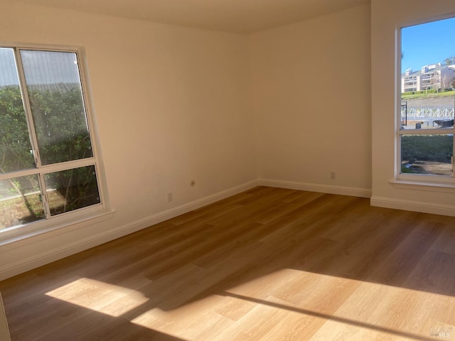 unfurnished room featuring plenty of natural light, baseboards, and wood finished floors