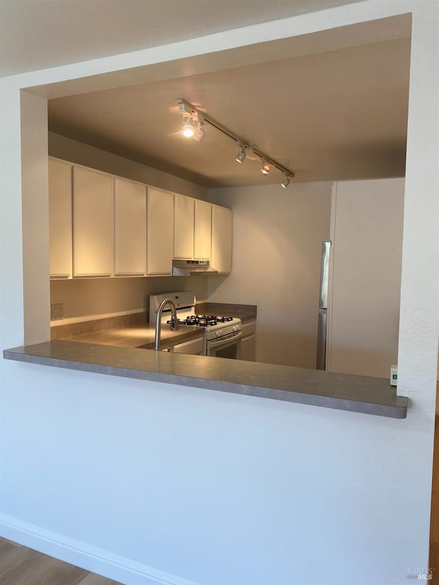 kitchen featuring white range with gas stovetop, a sink, under cabinet range hood, and a peninsula