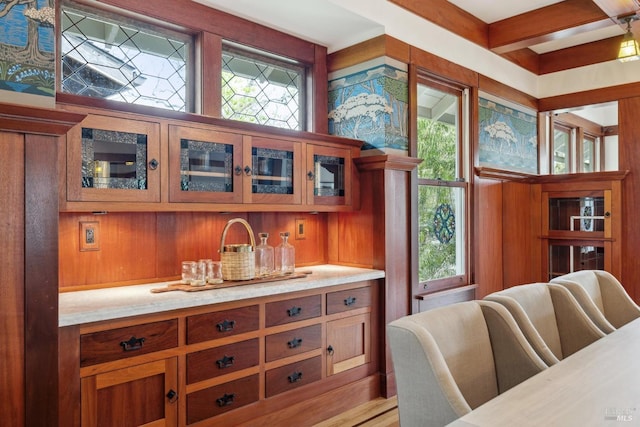 kitchen with glass insert cabinets, brown cabinetry, and light stone counters