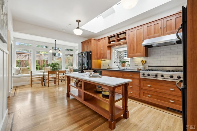 kitchen with under cabinet range hood, stainless steel gas cooktop, a skylight, freestanding refrigerator, and open shelves