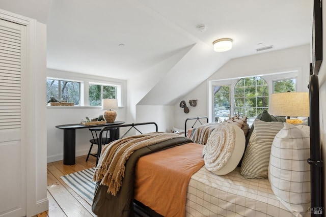 bedroom with baseboards, visible vents, vaulted ceiling, and wood finished floors