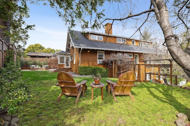 back of house featuring entry steps, roof with shingles, a chimney, and a yard