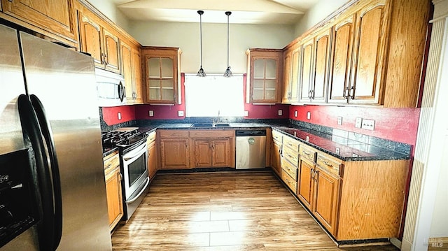 kitchen with dark countertops, light wood-style flooring, appliances with stainless steel finishes, and glass insert cabinets