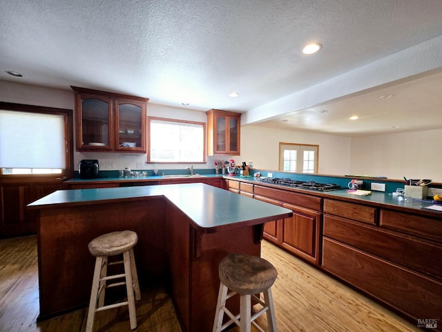 kitchen featuring stainless steel gas cooktop, a center island, light wood-style flooring, and a kitchen breakfast bar