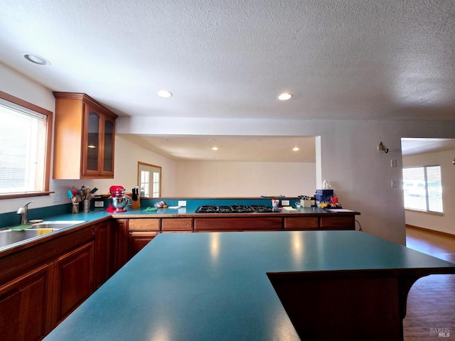 kitchen with glass insert cabinets, black gas stovetop, a textured ceiling, a sink, and recessed lighting