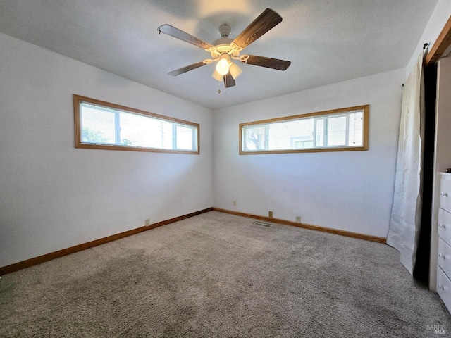 carpeted empty room with visible vents, ceiling fan, and baseboards