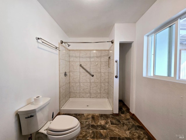 full bath with stone finish floor, tiled shower, baseboards, and toilet