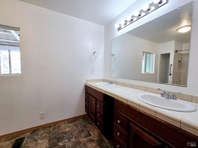 full bathroom with double vanity, stone finish flooring, baseboards, and a sink