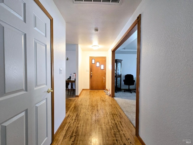 hallway featuring baseboards, visible vents, wood finished floors, and a textured wall