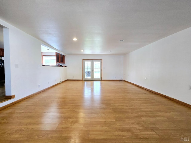 spare room featuring light wood finished floors, french doors, and baseboards