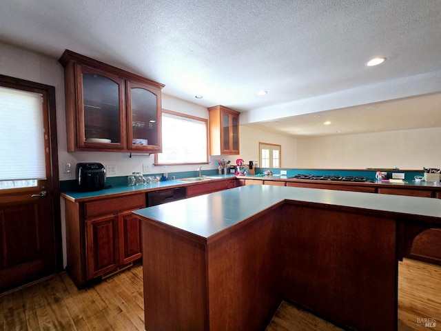 kitchen with light wood-style floors, glass insert cabinets, a kitchen island, a textured ceiling, and dishwasher