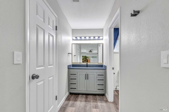 bathroom with a textured wall, wood finished floors, vanity, and baseboards