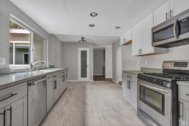 kitchen with arched walkways, stainless steel appliances, visible vents, white cabinetry, and a textured ceiling