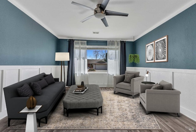 living room featuring a ceiling fan, a wainscoted wall, visible vents, and wood finished floors