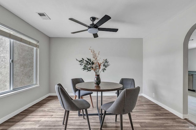 dining space featuring arched walkways, visible vents, baseboards, and wood finished floors