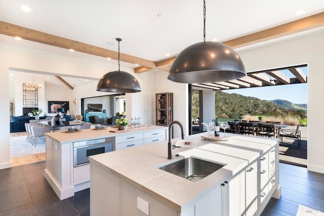 kitchen with an island with sink, open floor plan, light countertops, white cabinetry, and a sink