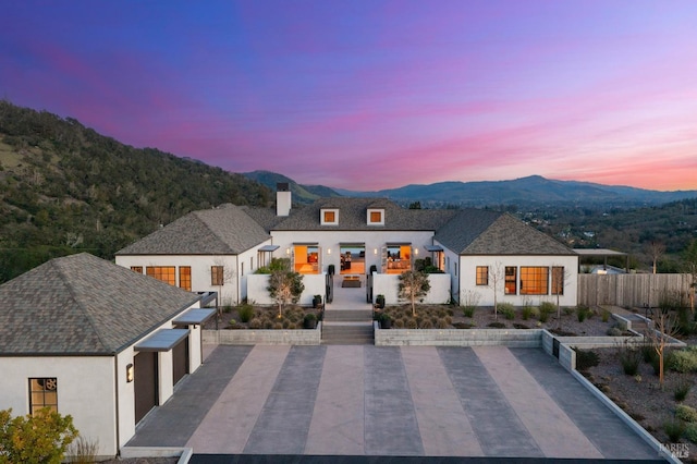 back of property at dusk featuring a chimney, a mountain view, fence, and stucco siding