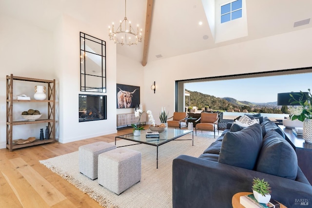 living area featuring high vaulted ceiling, a mountain view, wood finished floors, beamed ceiling, and a glass covered fireplace