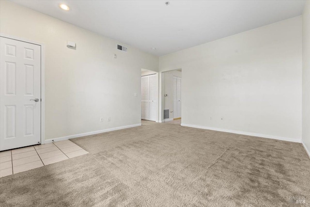 unfurnished room featuring light carpet, light tile patterned floors, visible vents, and baseboards