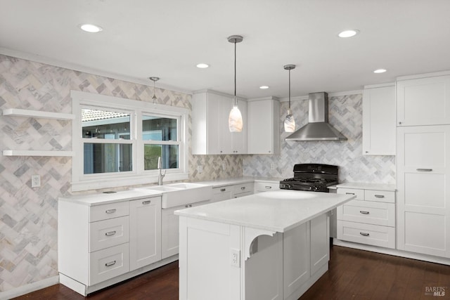 kitchen with black gas range, white cabinets, light countertops, wall chimney range hood, and a sink