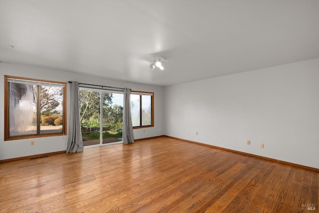 empty room with light wood-style floors, visible vents, and baseboards